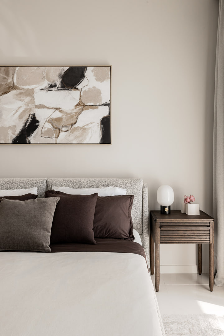 Upholstered bed with dark cushions, timber bedside table and abstract art
