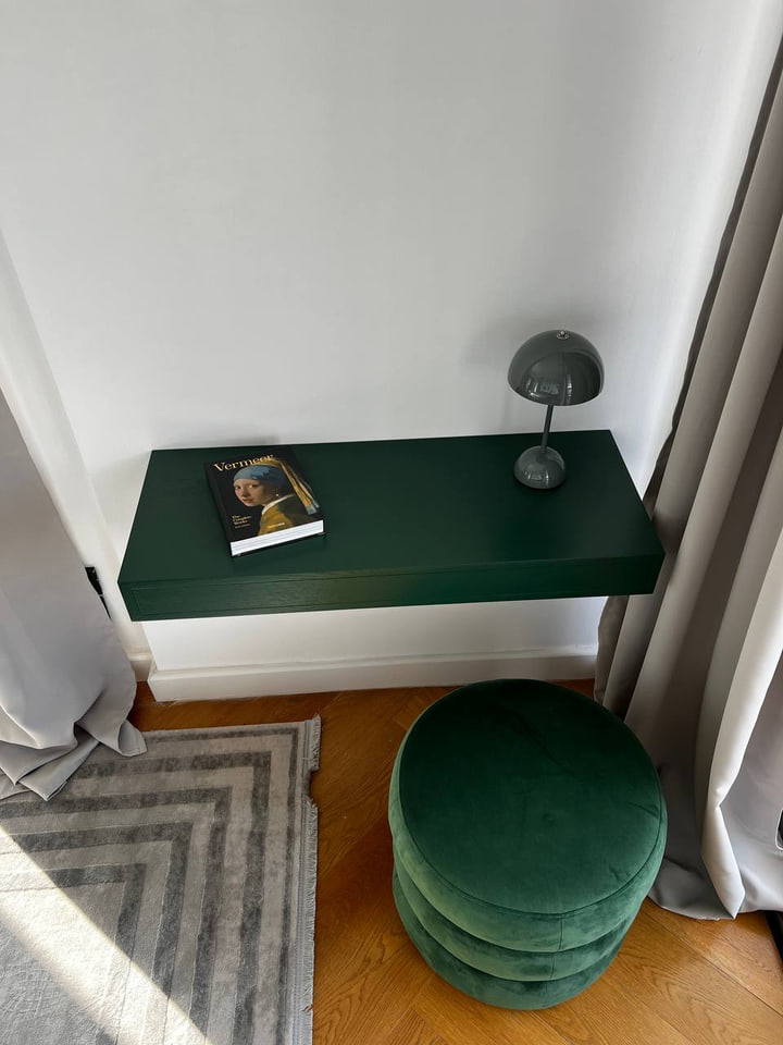 Deep green floating desk with a round velvet stool by the window