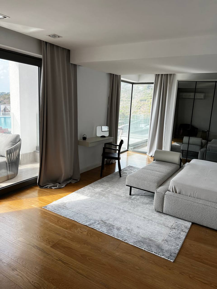 Spacious bedroom with upholstered bed, chaise and windows towards the landscape